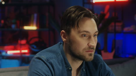 Close-Up-Of-The-Attractive-Young-Man-Turning-His-Head-To-The-Camera-And-Smiling-Cheerfully-In-The-Dark-Room-At-Night