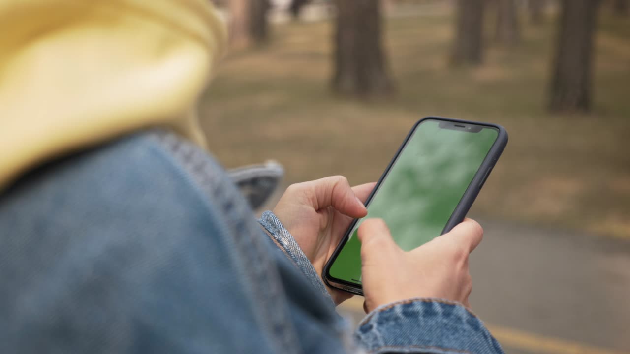 Woman works on smartphone in city park, close up on hands. Female using mobile phone in public park to communicate with others, use mobile apps. Mobile technology and communication. Chroma key screen
