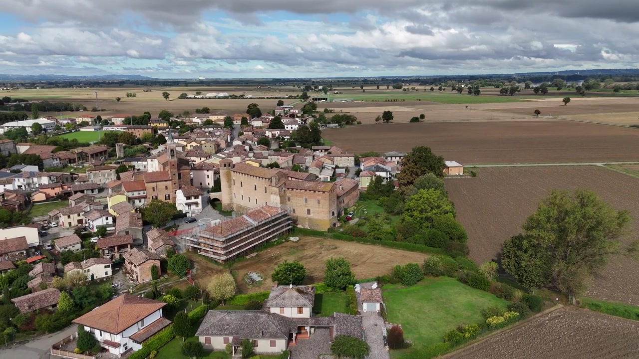 Ripresa aerea con drone sopra il Castello di Calendasco vicino a Piacenza, Emilia Romagna, Italia, che rivela l'architettura di una fortezza medievale, il tessuto del villaggio rurale e i terreni agricoli coltivati della Pianura Padana.