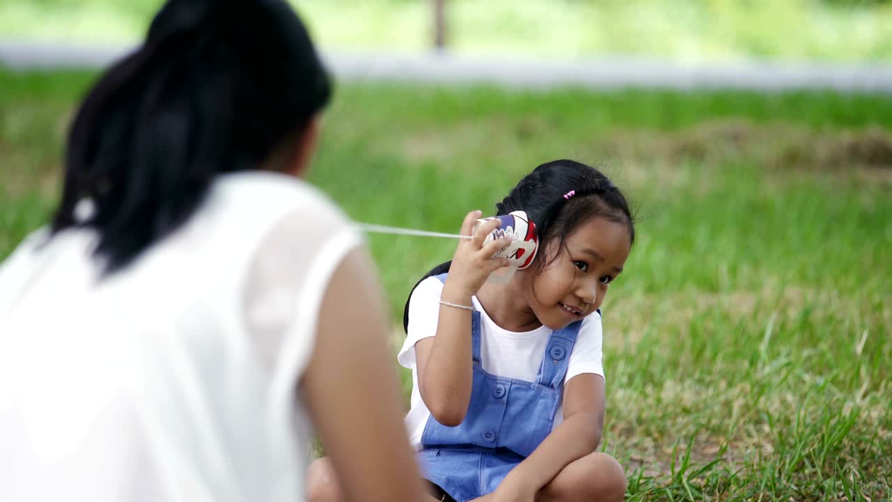 Asian family, mother and daughter doing string phone play activities tie rope at the park.