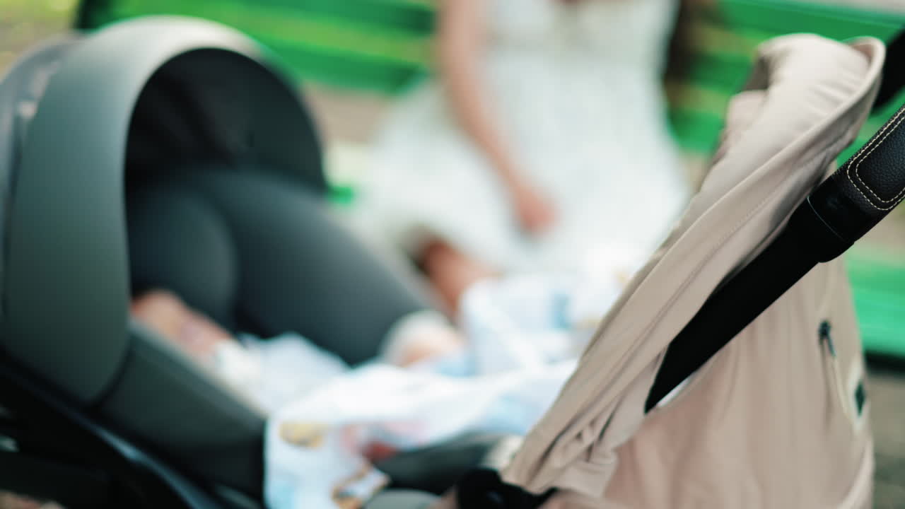 A baby resting in a stroller while a woman sits on a green bench in the background