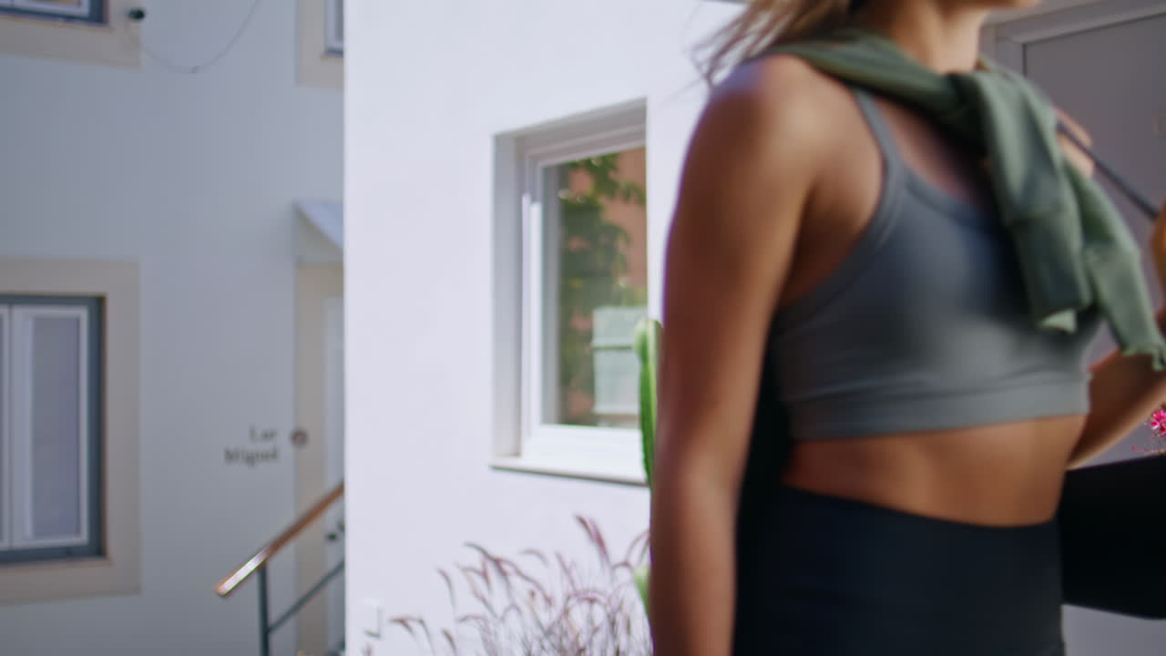 Active woman walking outdoors carrying yoga mat in residential area. Happy lady