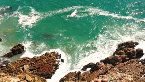 rocky coastline with turqoise waves breaking into rocks, aerial drone view