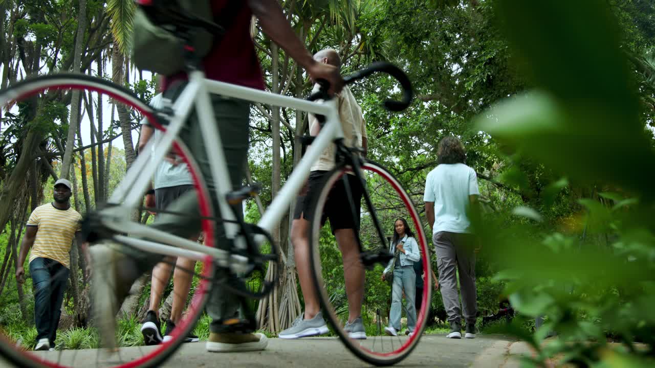 Due uomini in pantaloncini si preparano a correre su un sentiero del parco, riparandosi gli occhi, gesticolando, facendo jogging sotto la chioma degli alberi.