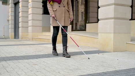 mid view of a blind woman in brown coat and black boots walking with a walking stick in the street 1