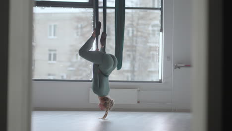 young smiling woman practice in aero stretching swing. aerial flying yoga exercises practice in green hammock in fitness club