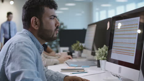 Side-View-Of-Workers-Working-At-Desk-In-Front-Of-Computer-In-Office