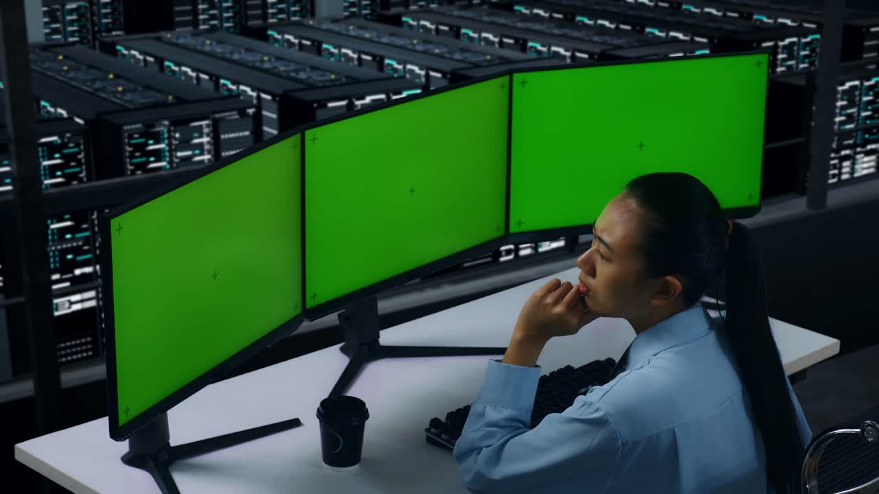 vista laterale di una donna asiatica che pensa a qualcosa mentre lavora con un monitor di computer simulato in un centro dati
