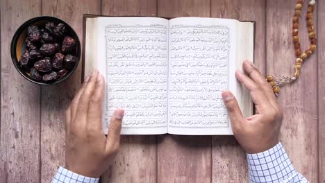 muslim man hand turning pages of holly book of quran top view