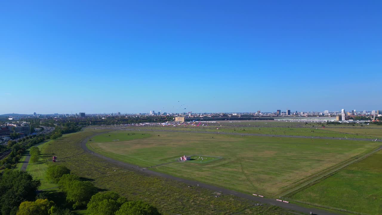 thousands of Berliners enjoying the giant kite festival on a sunny day at Tempelhofer Feld, the former Tempelhof Airport. Magic aerial view flight ascending drone