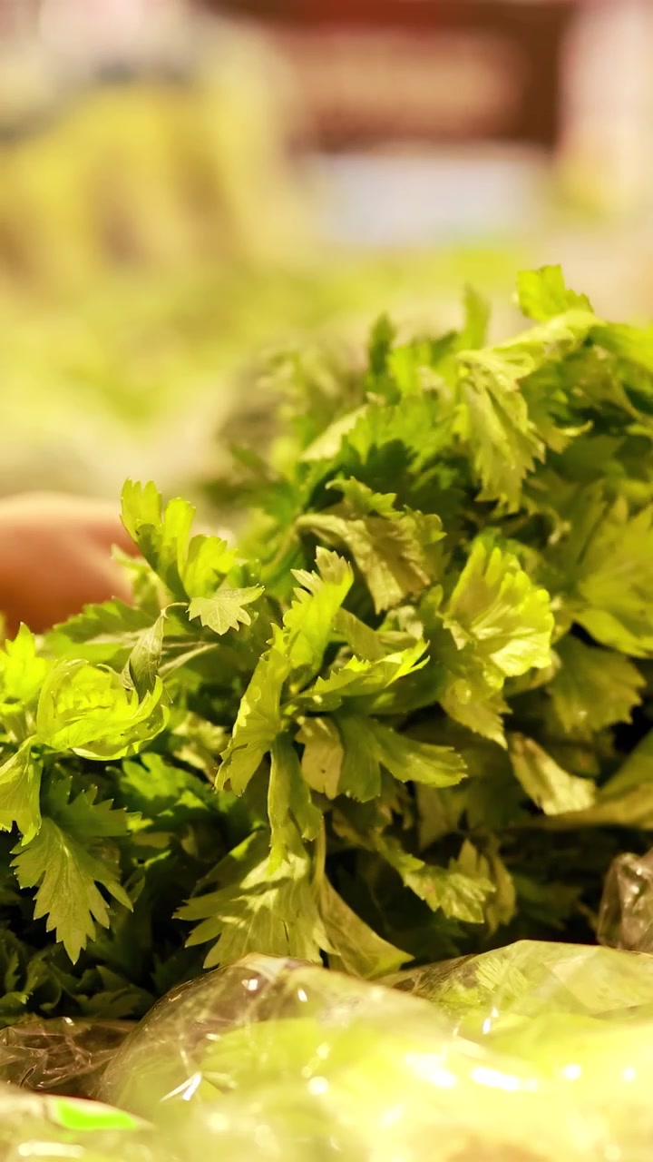 A hand examines fresh celery in a well-lit supermarket, highlighting vibrant greens and crisp textures