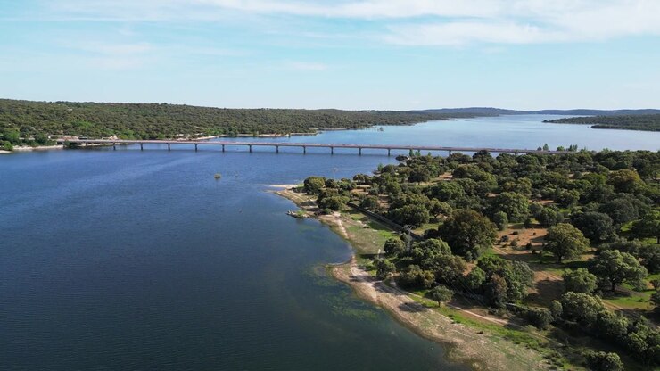 Un ponte attraversa un ampio bacino idrico con sponde verdi lussureggianti e cieli sereni. Ideale per documentari ambientali o reportage di viaggio
