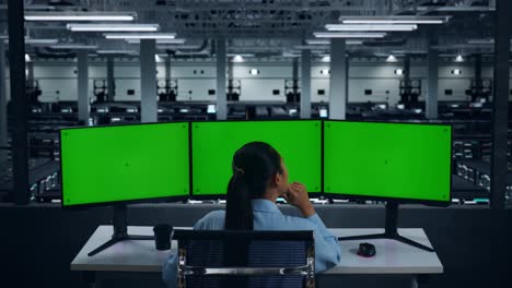vista trasera de una mujer asiática pensando en algo y luego levantando su dedo índice mientras trabaja con un simulacro de varios monitores de computadora en el centro de datos