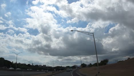 conduciendo por la autopista hacia honolulu en oahu hawaii con cielos brillantes y nubes y otros autos y camiones alrededor