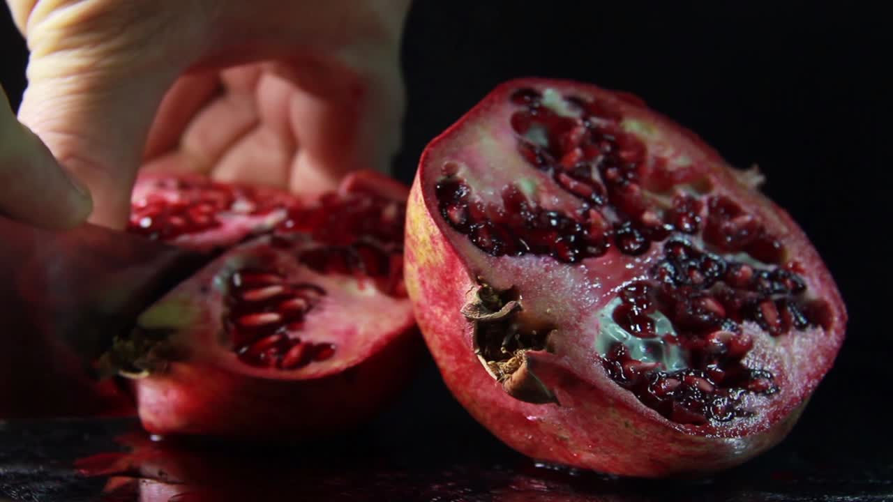 Skæring af granatæble med kniv på sort baggrund