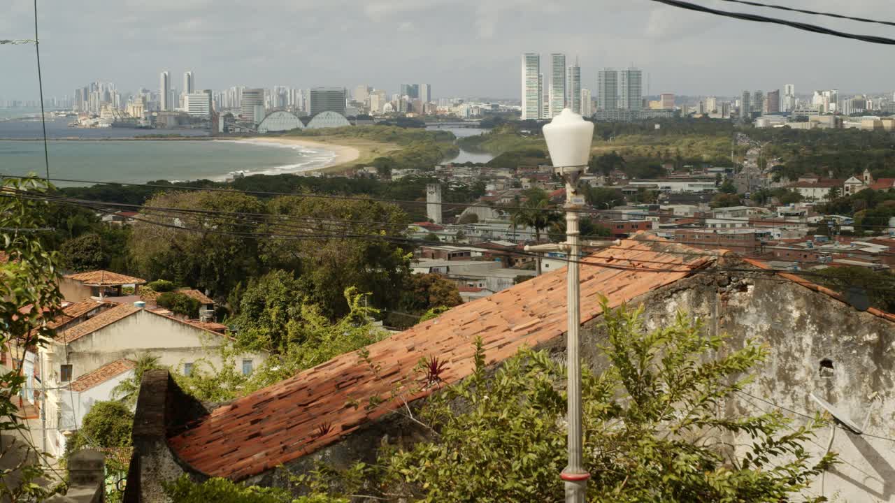 City landscape full of old houses, trees, ocean, small beach and buildings on the horizon on a cloud day