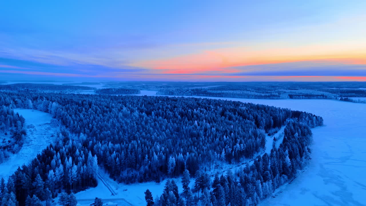 Luftfoto av en frossen innsjøhalvøy og vintersolnedgang. Bredt droneopptak av en snødekket skogkledd halvøy ved siden av et frossent vann.