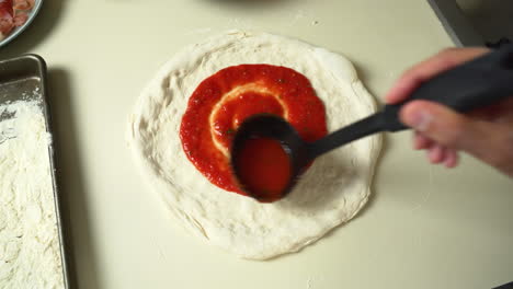 Top-view-of-Chef-while-spreading-Tomato-Sauce-on-Pizza-Dough-with-a-Ladle-in-Traditional-Italian-Pizza's-Restaurant
