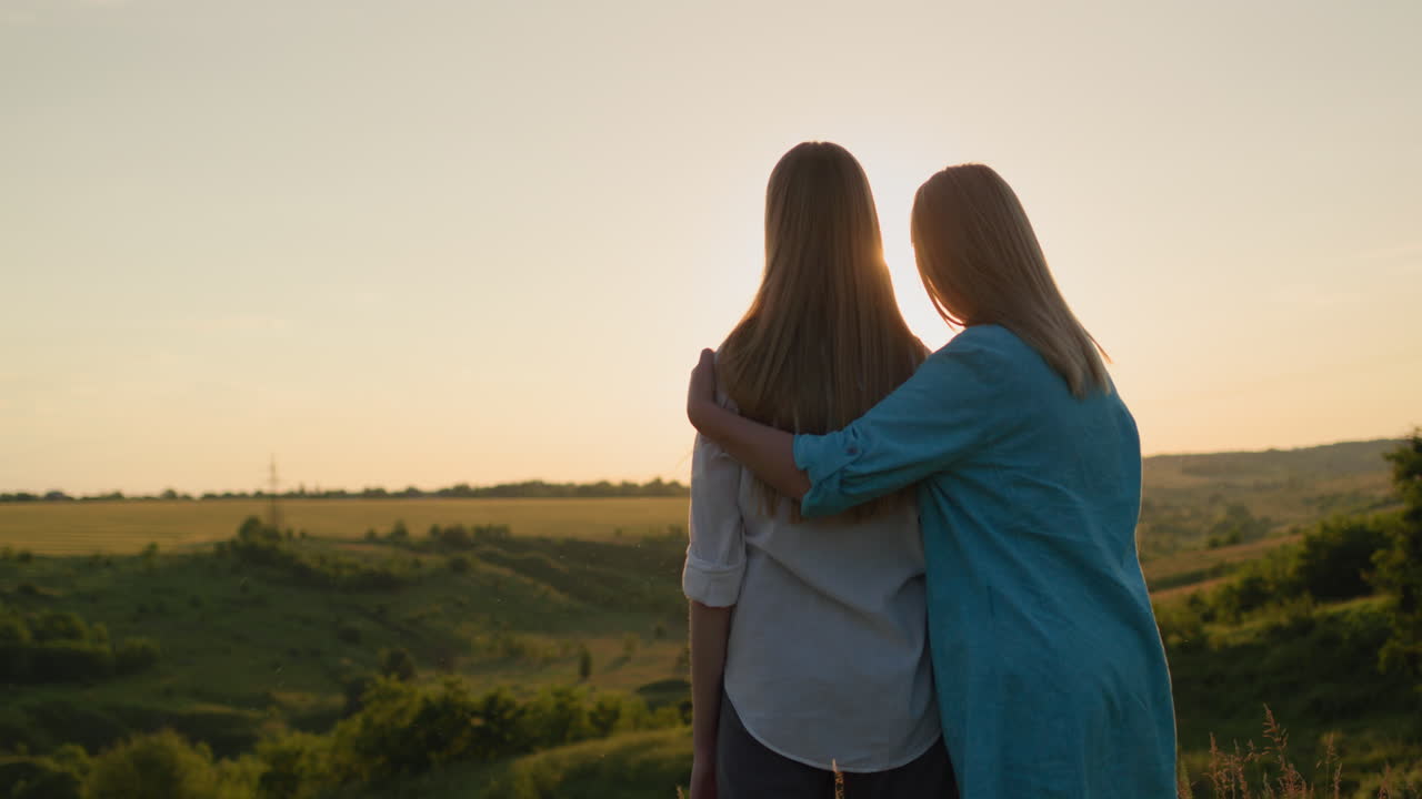 madre abraza a su hija adolescente, viendo la puesta de sol sobre un pintoresco valle. vista de atrás