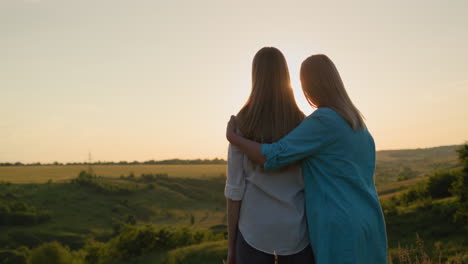 mom hugs her teenage daughter, watching the sunset over a picturesque valley. back view