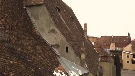 a drone shot, with a slant motion, capturing the rooftop, of a vintage architechture, with some residual snow on it, in the city of sighisoara on an afternoon