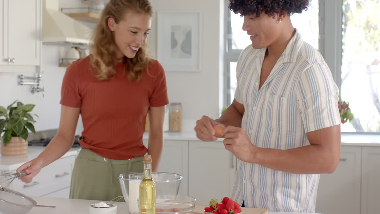 In kitchen, diverse couple preparing dessert with fresh strawberries, smiling together, at home