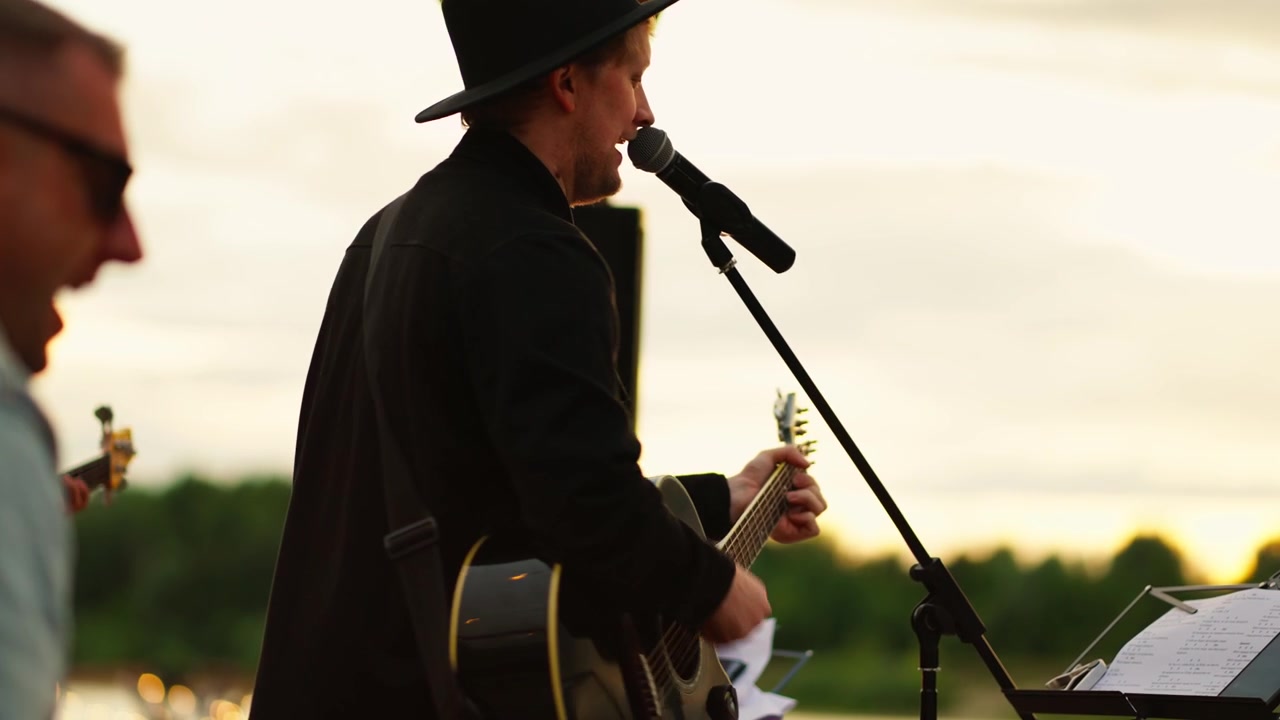 Musiker singt und spielt Akustikgitarre mit Band draußen bei Sonnenuntergang