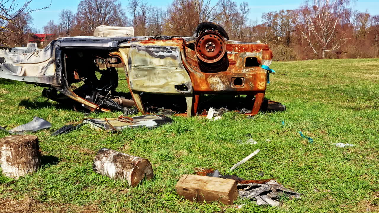 Rusted and burned car wreck flipped upside down in an open grassy field