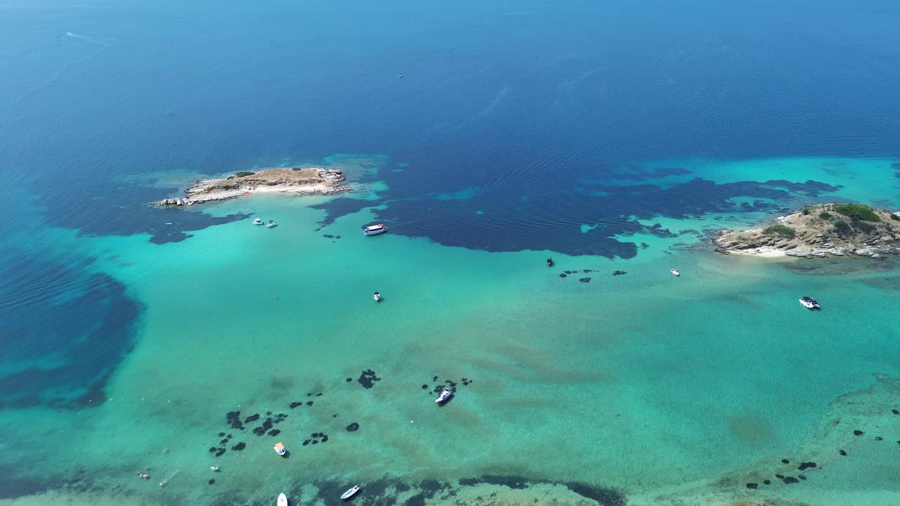 Vista aerea con drone delle spiagge turchesi delle Isole di Drenia vicino a Ouranoupoli, con acque cristalline e poco profonde, piccoli isolotti rocciosi e barche ancorate in estate