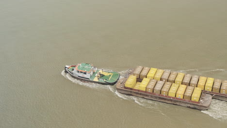 aerial view of tug boat towing cargo of shipping containers on river thames