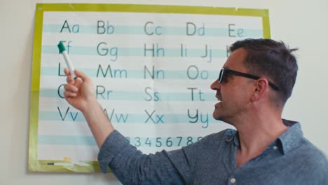 European Caucasian white male man English language teacher tutor in glasses teaches and explains English alphabet