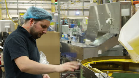 Factory-worker-inspects-vibratory-bowl-feeder-at-indoor-industrial-plant,-medium