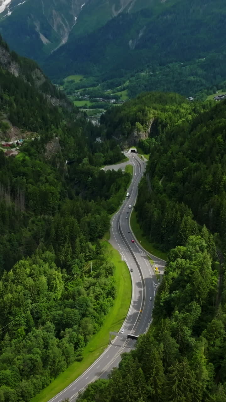 Vertical drone shot tilting over a road, revealing snowy mountains of Chamonix