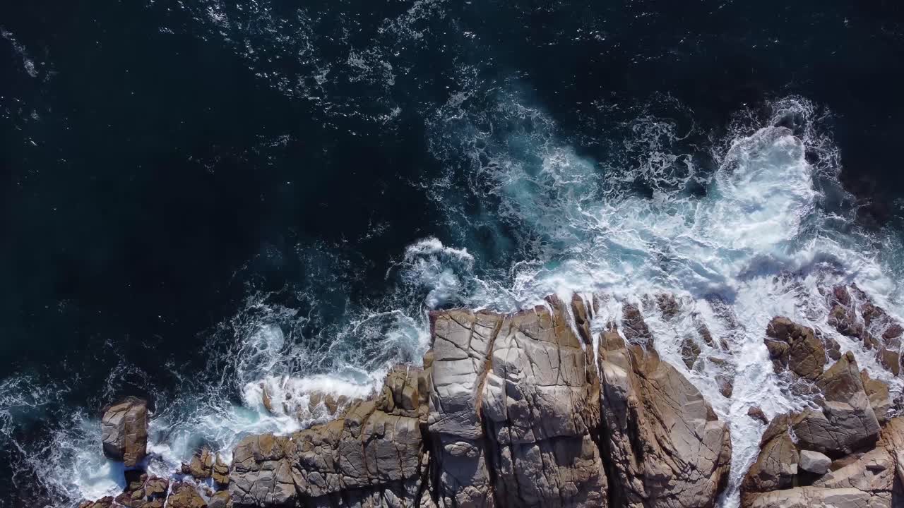 olas espumosas del mar salpicando en la costa rocosa a la luz del sol