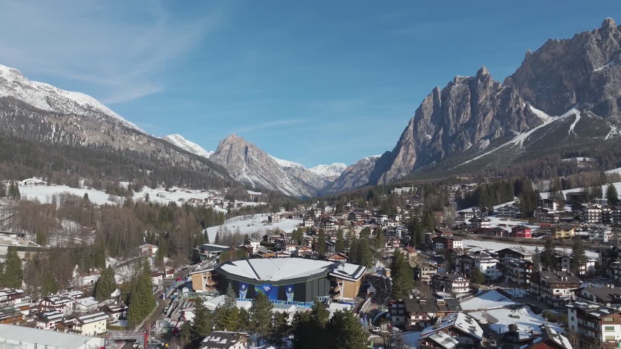 Scenic view of the alpine town and surrounding Dolomites mountains under a blue sky. Cortina d'Ampezzo, Italy. Sunny day. Aerial