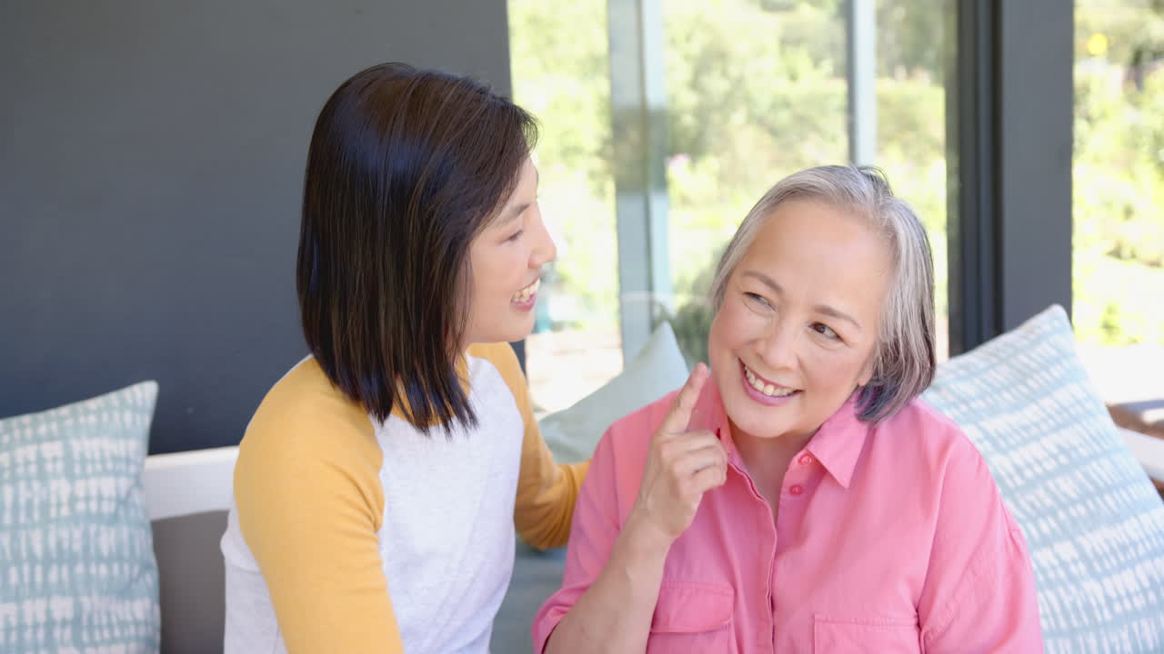 Smiling senior asian woman receiving affectionate care from younger asian woman at home