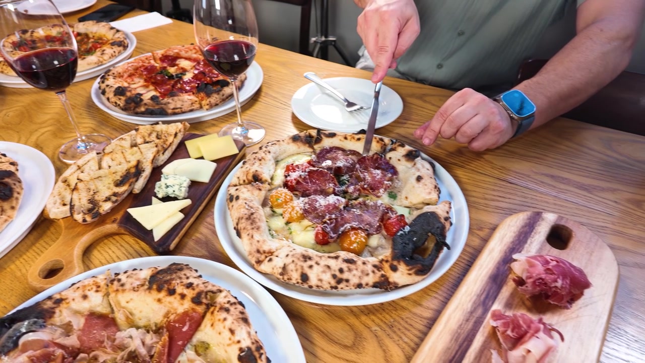 Ahşap bir masa üzerinde İtalyan pizzaları, şarap ve mezeleri paylaşan insanların yüksek açılı çekimi.