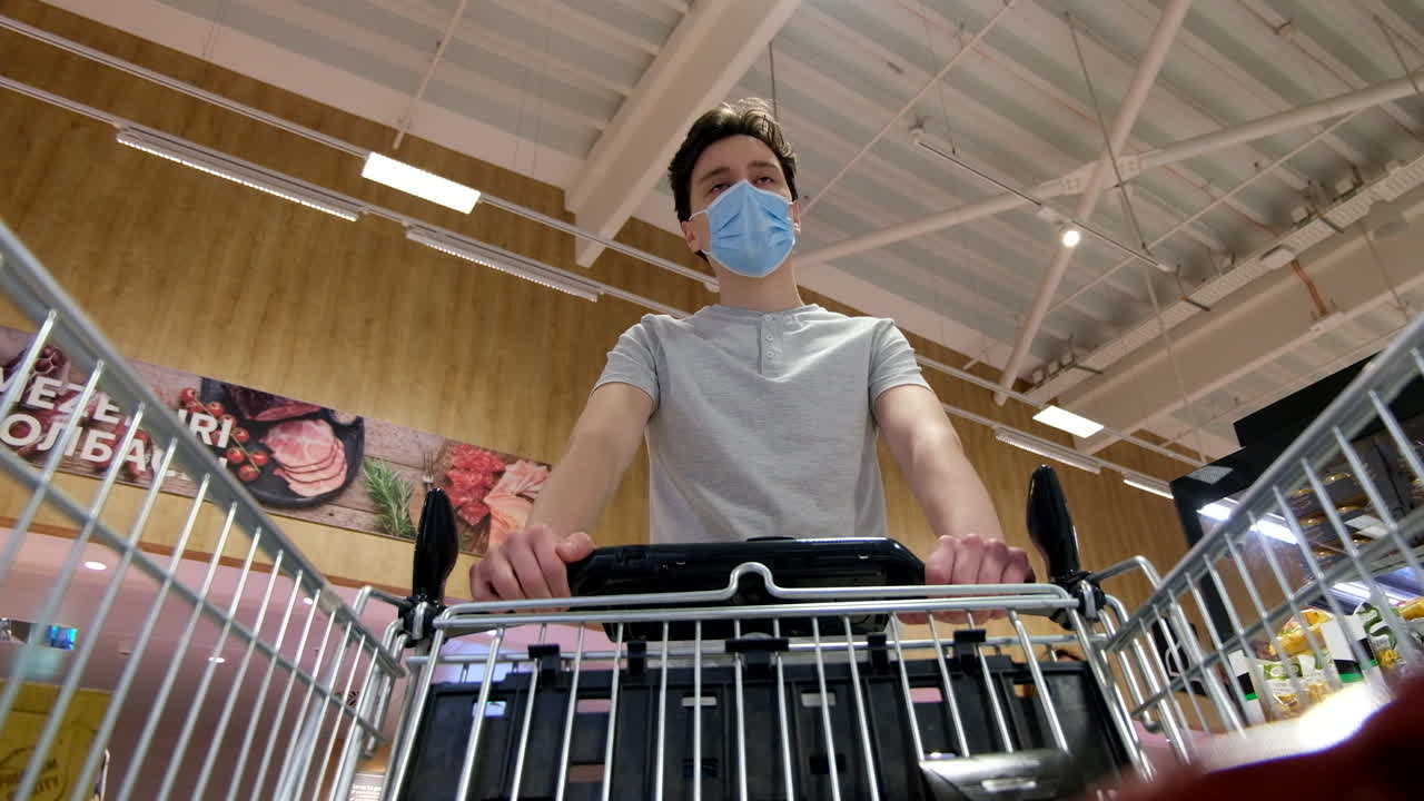 CHISINAU, MOLDOVA - JUNE 5, 2020: Timelapse of a young man with a protective medical mask walking in a supermarket and looking around. View from the cart. Corona Virus idea