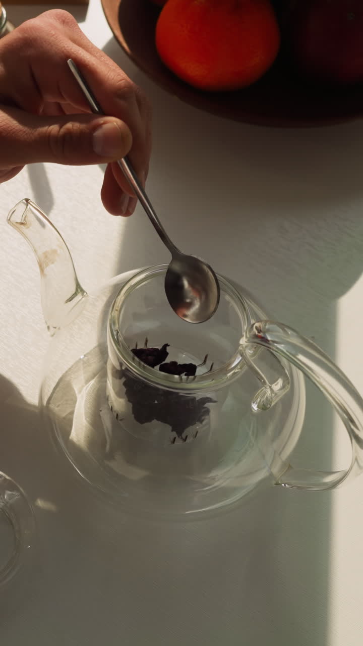 el marido pone hojas de té en una tetera de vidrio. comida matutina nutritiva cerca de la ventana acompañada de té y frutas frescas. organización de los elementos esenciales del té