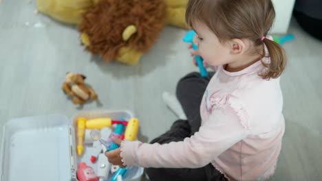 little girl with pigtails playing doctor using toy plastic tools to check ears