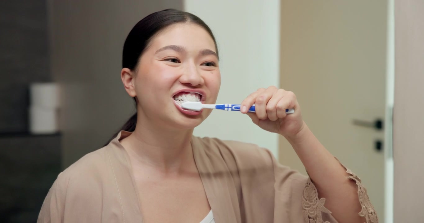 Young Woman Brushing Her Teeth in Front of a Bathroom Mirror
