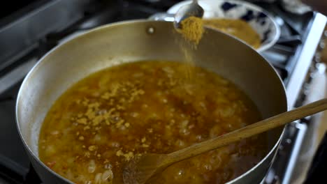 spices being added to simmering curry sauce from spoon into large pot