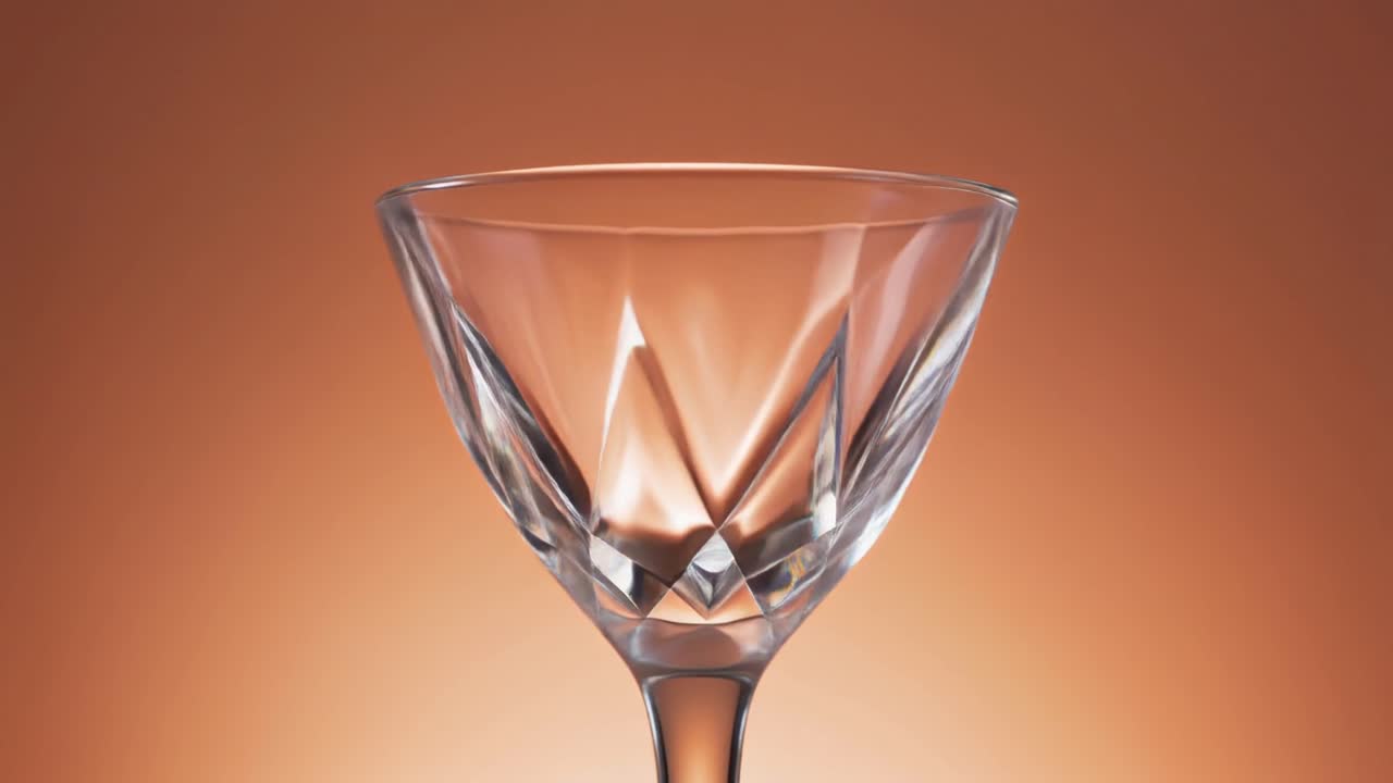 Elegant tomt cocktailglas med facetslebet design på varm baggrund