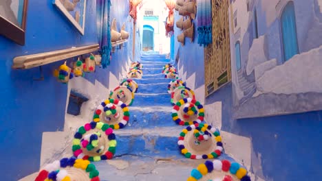 Subiendo-Una-Escalera-Pintoresca-Pov-Con-Coloridos-Sombreros-De-Paja-En-Las-Paredes-Azules,-Chefchaouen