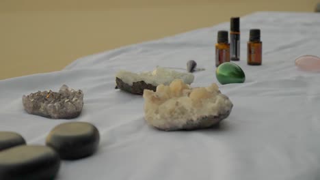 equipment for massage placed on massage table covered with white cloth - crystals, aromatic oils, stone and yoni eggs