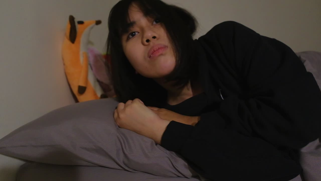 꿈꾸는 아시아 소녀는 침대에 누워 있고,  ⁇ 어낸 장난감과 함께 깨어 있습니다.