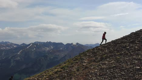 Female-hiker-walks-up-rocky-mountain-ridge-in-the-mountains