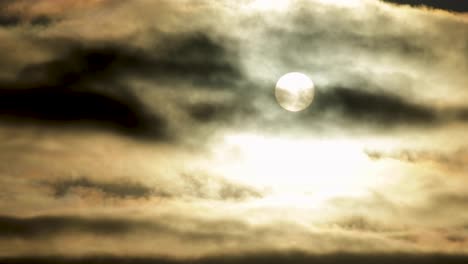 fog moves across a full moon framed against a dark moody, amber sky with cloud cover