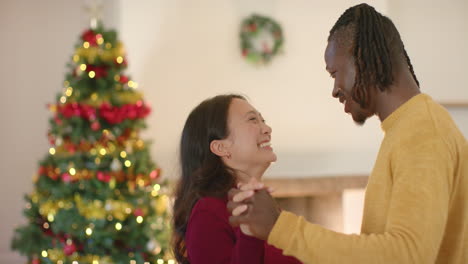 Feliz-Pareja-Diversa-Bailando-Junto-Al-árbol-De-Navidad-En-Casa,-Cámara-Lenta