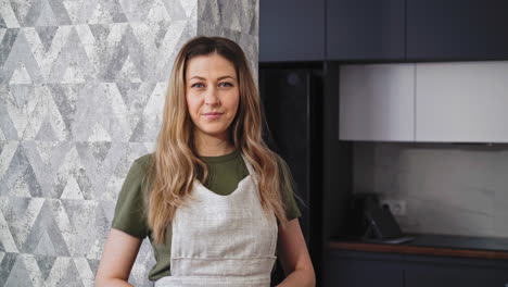 mujer en delantal gris se encuentra cerca de la pared decorada en la cocina